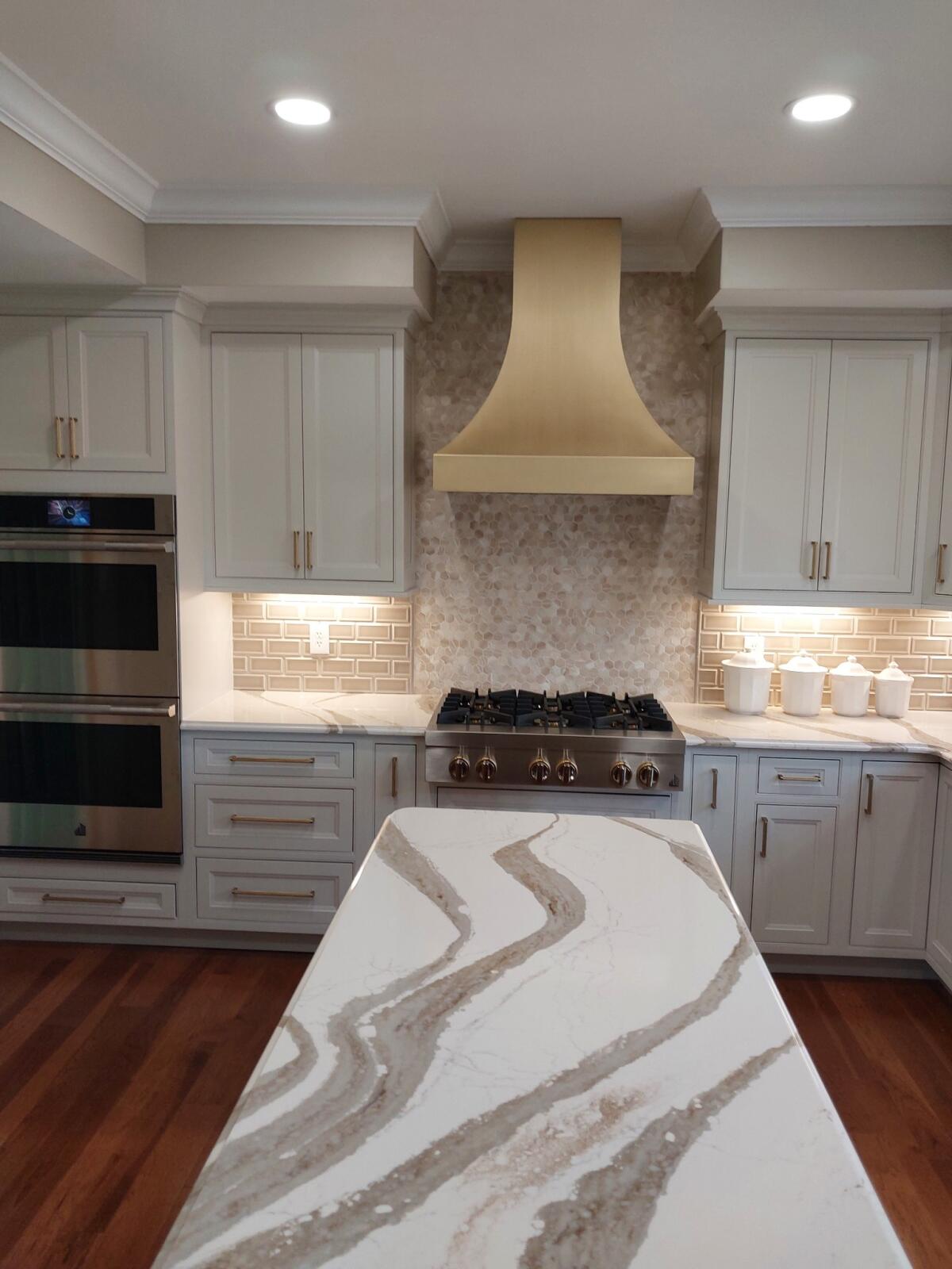 Classic kitchen with white cabinets, marble countertops, brick backsplash, enhanced by a sleek range hood, exudes timeless elegance
