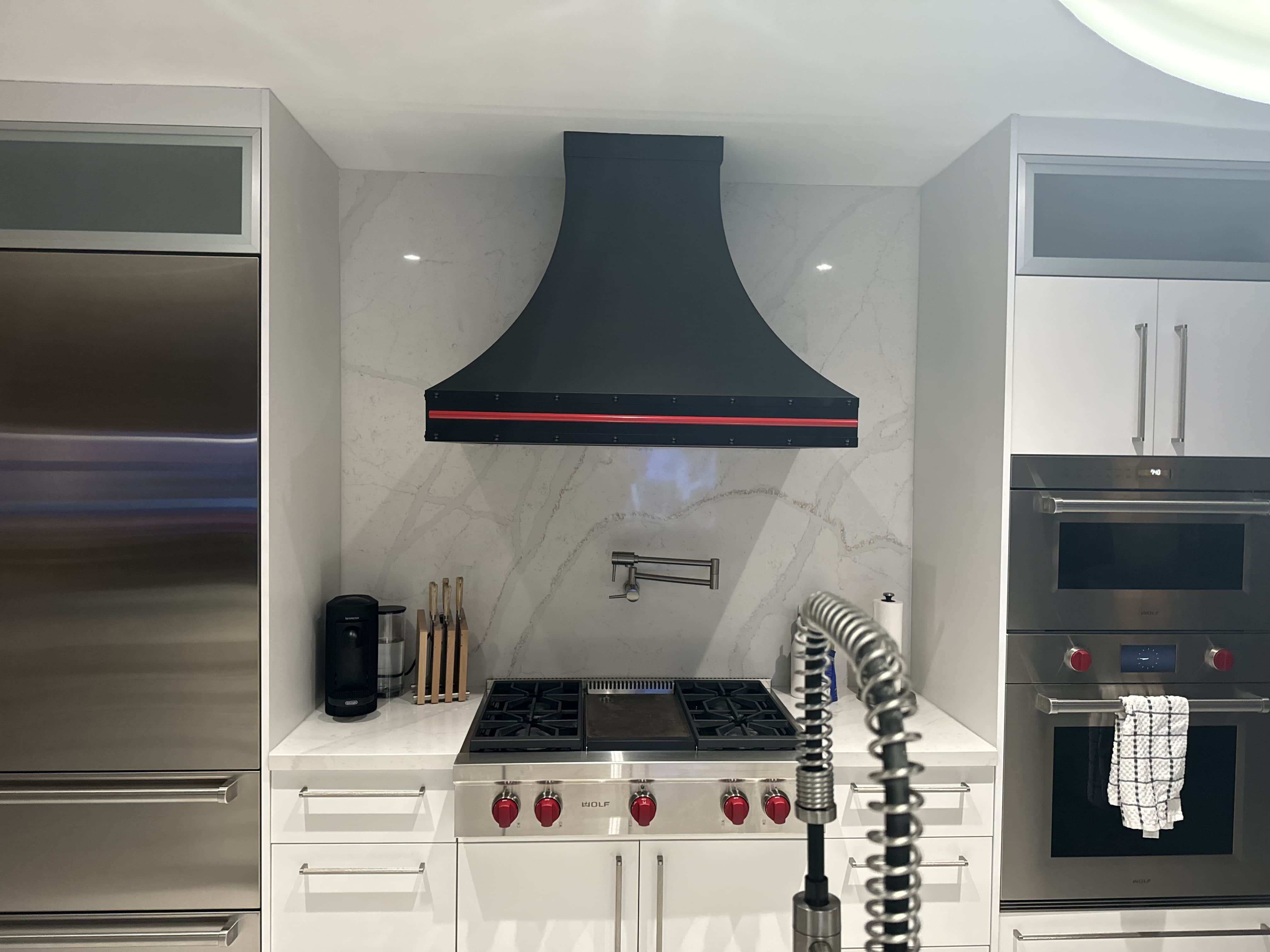 CopperSmith Euro ES3 Wall Mount Stainless Steel Black Enamel with RAL 3001 Signal Red Rivets and Pot Rail in a modern kitchen with Marble Backsplash , white countertops and cabinets