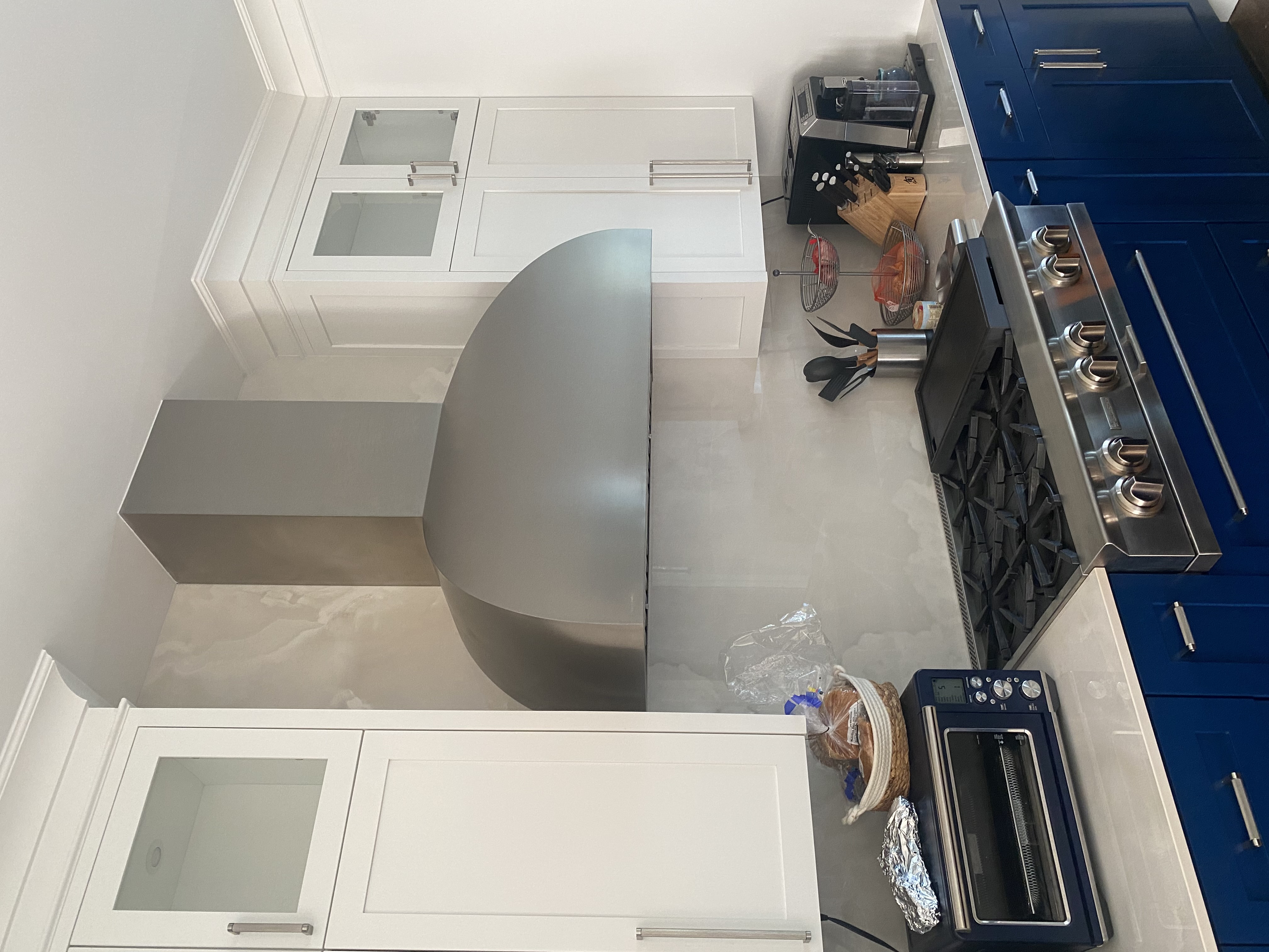 A coastal kitchen project featuring blue kitchen cabinets, marble kitchen countertops, marble backsplash with a sleek range hood design