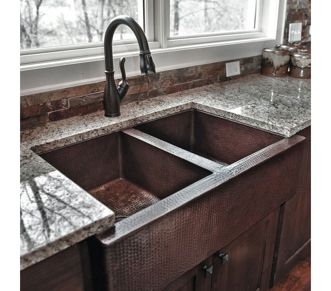 Copper hammered sink in a kitchen with dark wood cabinets and a tile backsplash World CopperSmith.