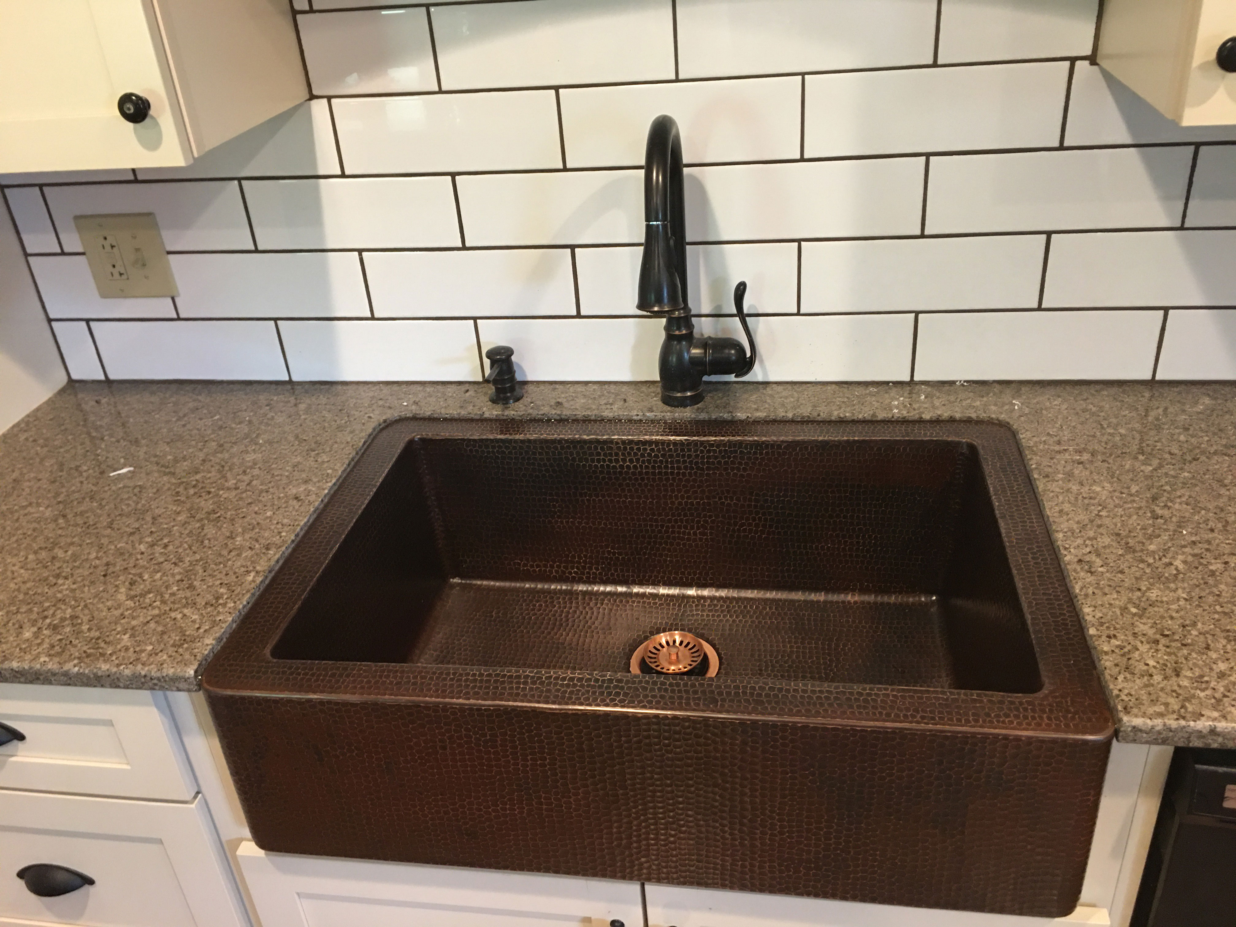 Copper apron front sink in a kitchen with white cabinets and a dark copper finish World CopperSmith.