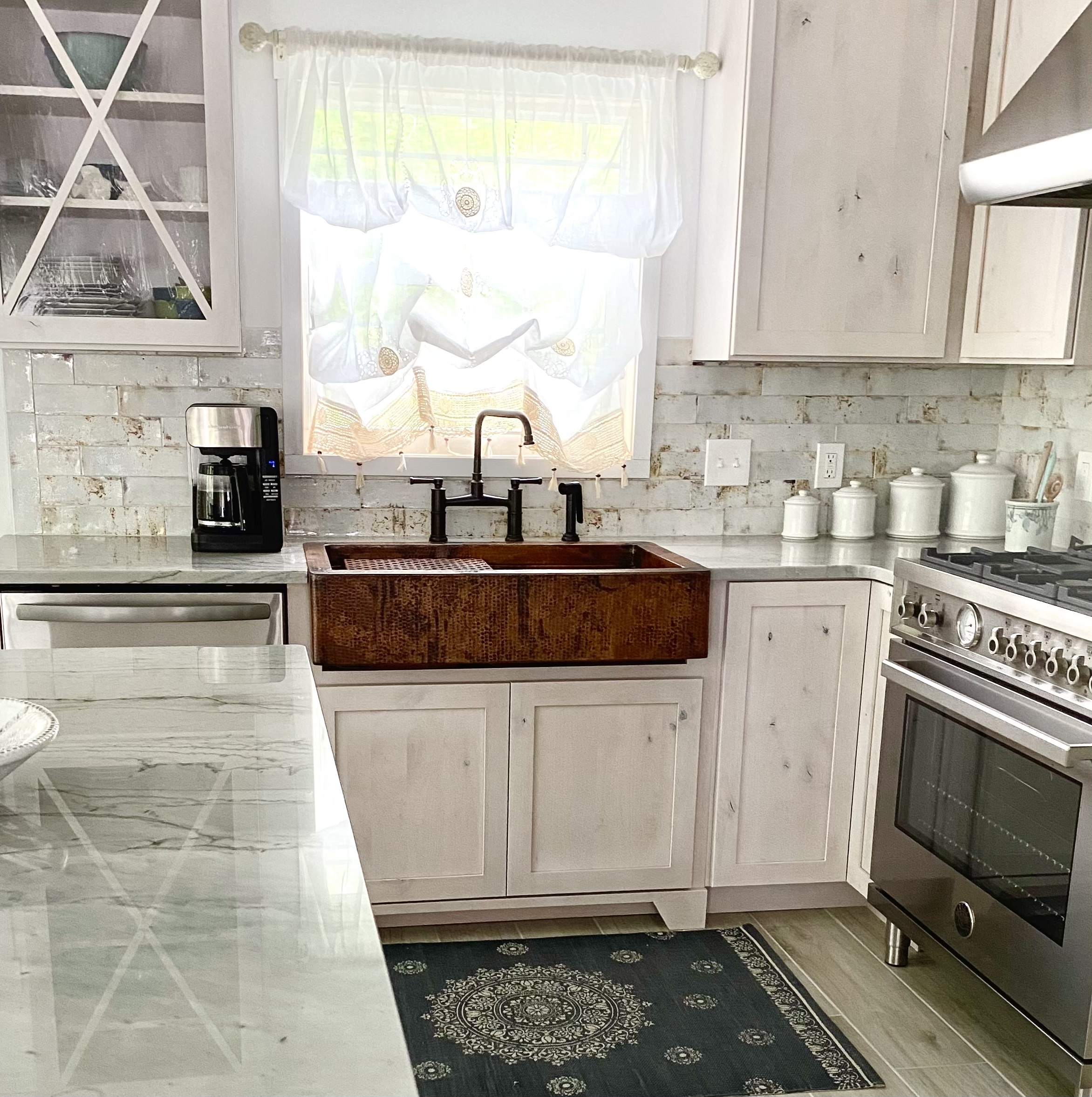 Imposing coastal kitchen with white kitchen cabinets, marble kitchen countertops, a stylish range hood, captivating brick backsplash