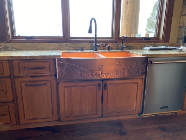 Modern kitchen design with a farmhouse sink, craftsman-style cabinets in rich brown, elegant marble countertops, stunning copper backsplash