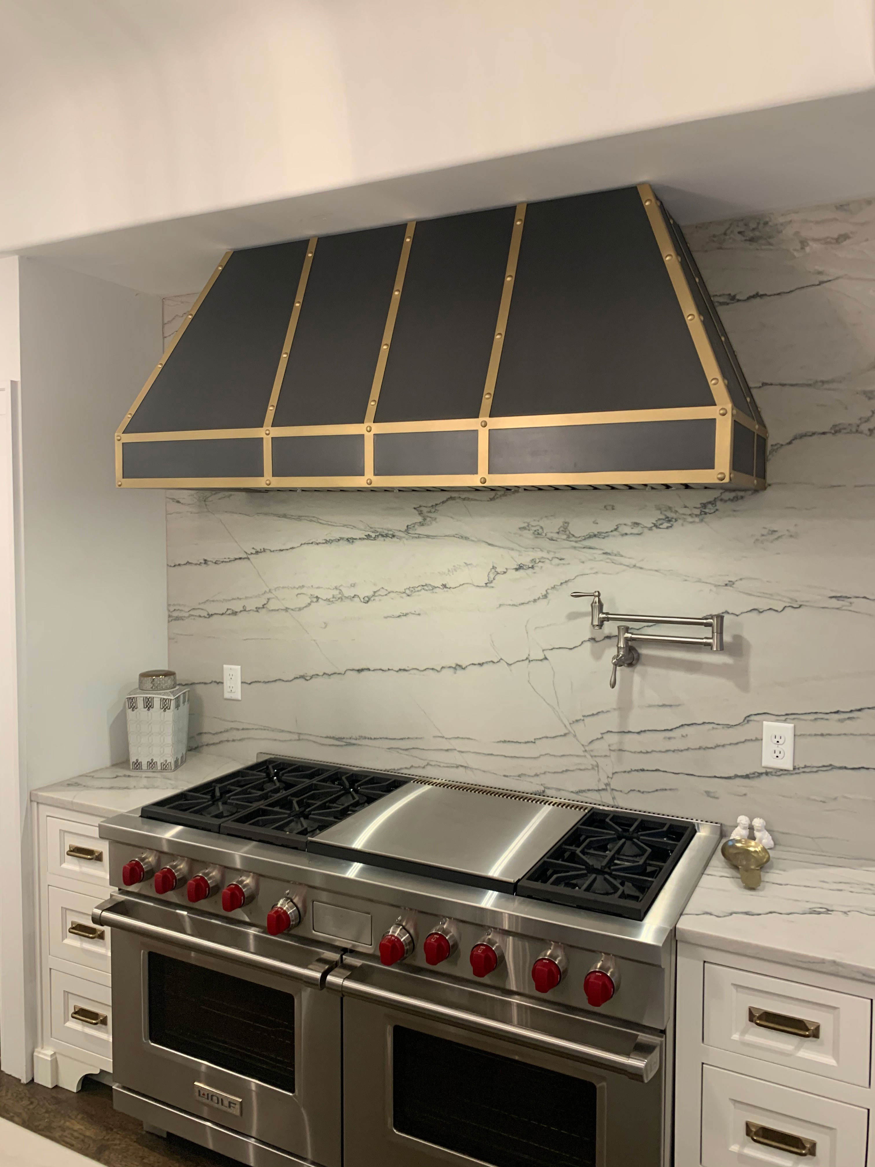 Timeless kitchen design idea with stylish range hood, including white kitchen cabinets, white countertops and marble backsplash