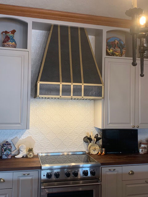 Black and brass range hood in kitschy kitchen with white cabinets World CopperSmith
