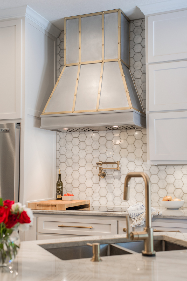 Kitchen design highlighted with range hood by white cabinets with marble countertops and marble backsplash