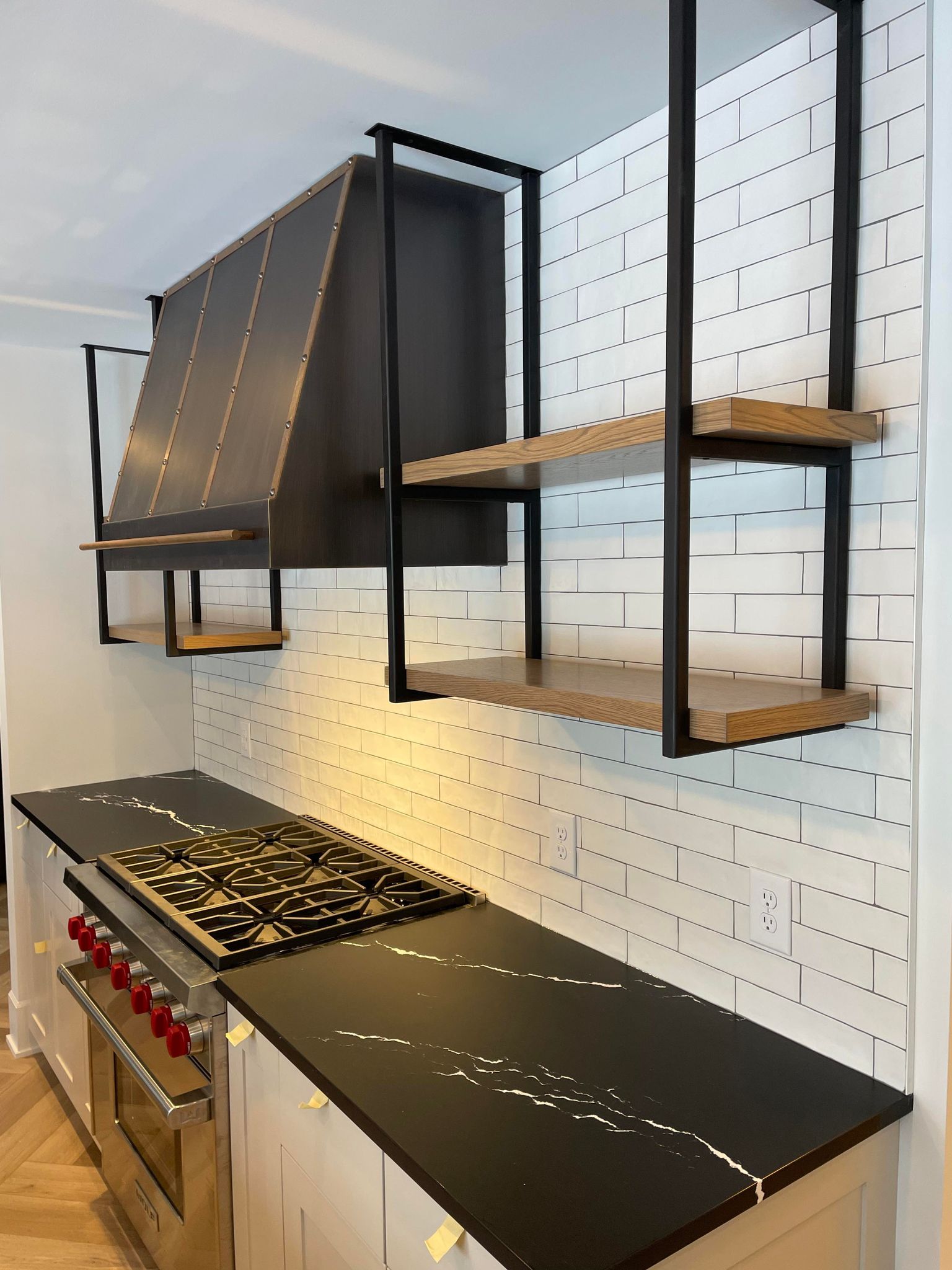 Sophisticated kitchen design idea, a french-inspired concept with white kitchen cabinets, black kitchen countertops, and white tile backsplash stylish range hood