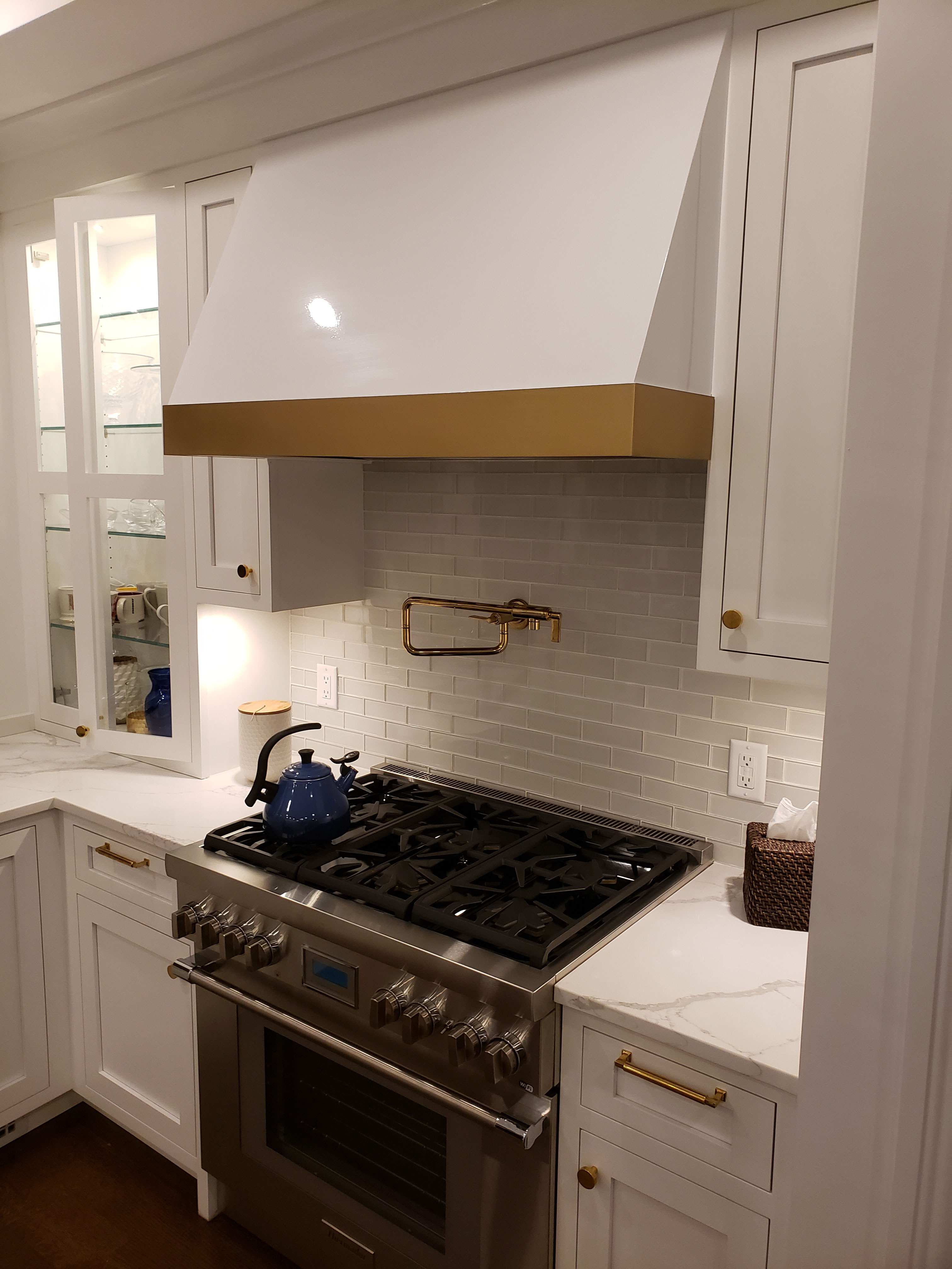 Beautiful cottage kitchen idea with stylish range hood, white kitchen cabinets and countertops, marble backsplash