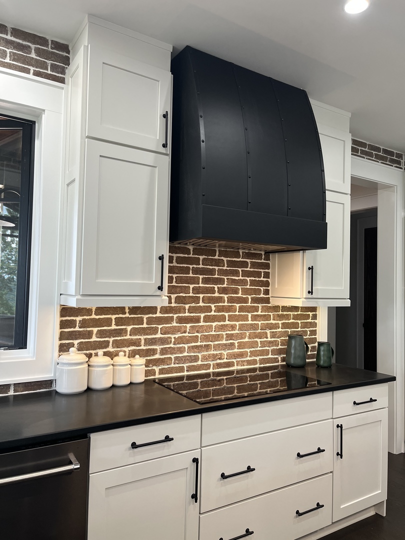 French kitchen design featuring range hood, white cabinets,black countertops captivating brick backsplash