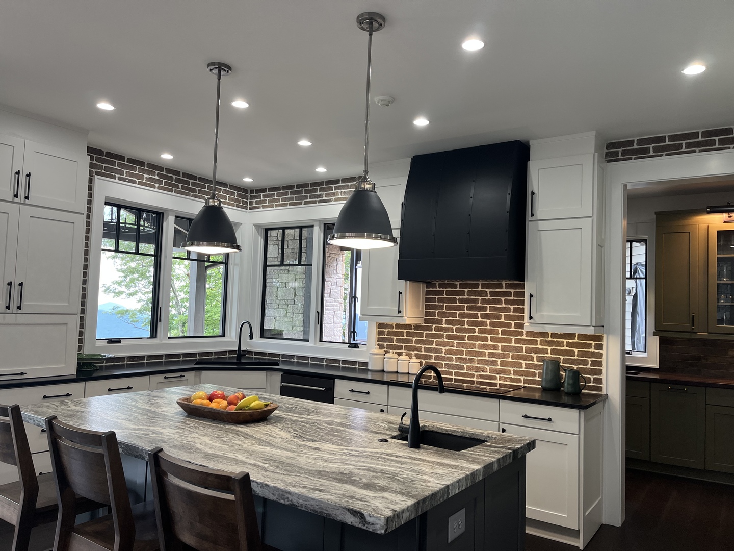 Great kitchen design with range hood, combining white cabinets,black countertops charming brick backsplash