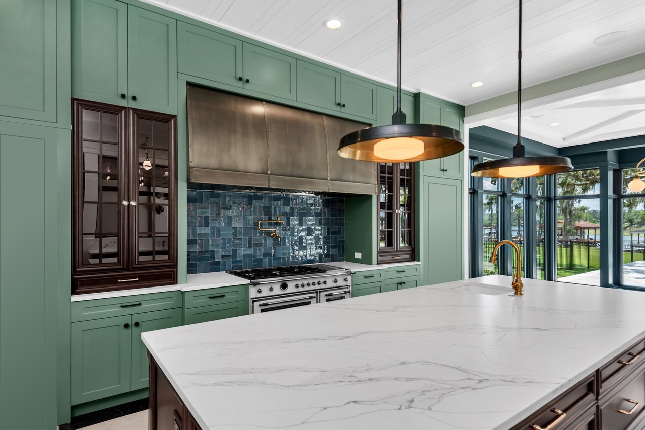 CopperSmith Premier PR4 Light Antique Brass Range Hood  in a Craftsman Style Kitchen with Green and wood cabinets white countertops and blue tile backsplash
