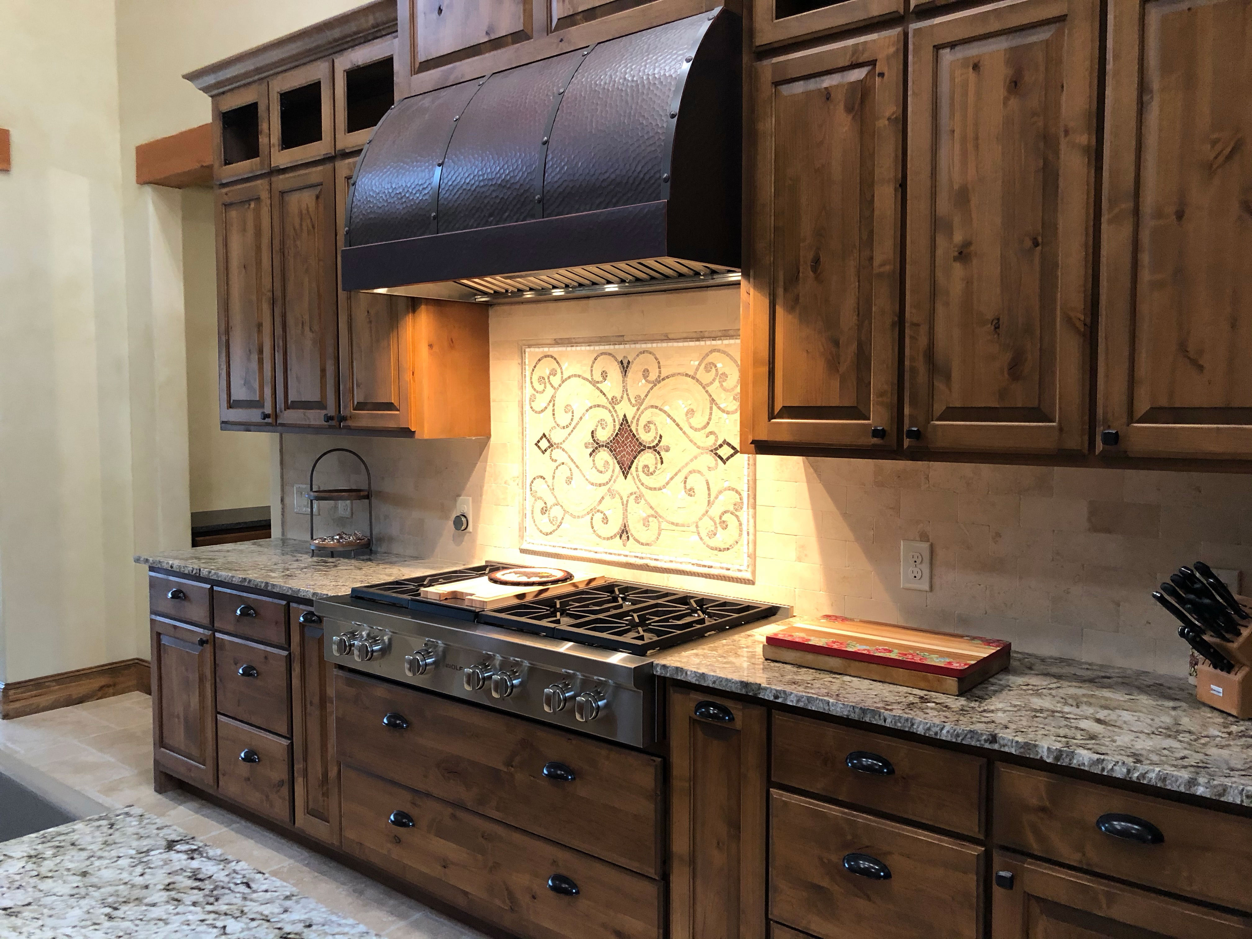 Stunning kitchen adorned enhances range hood, wood kitchen cabinets and marble kitchen countertops, brick backsplash
