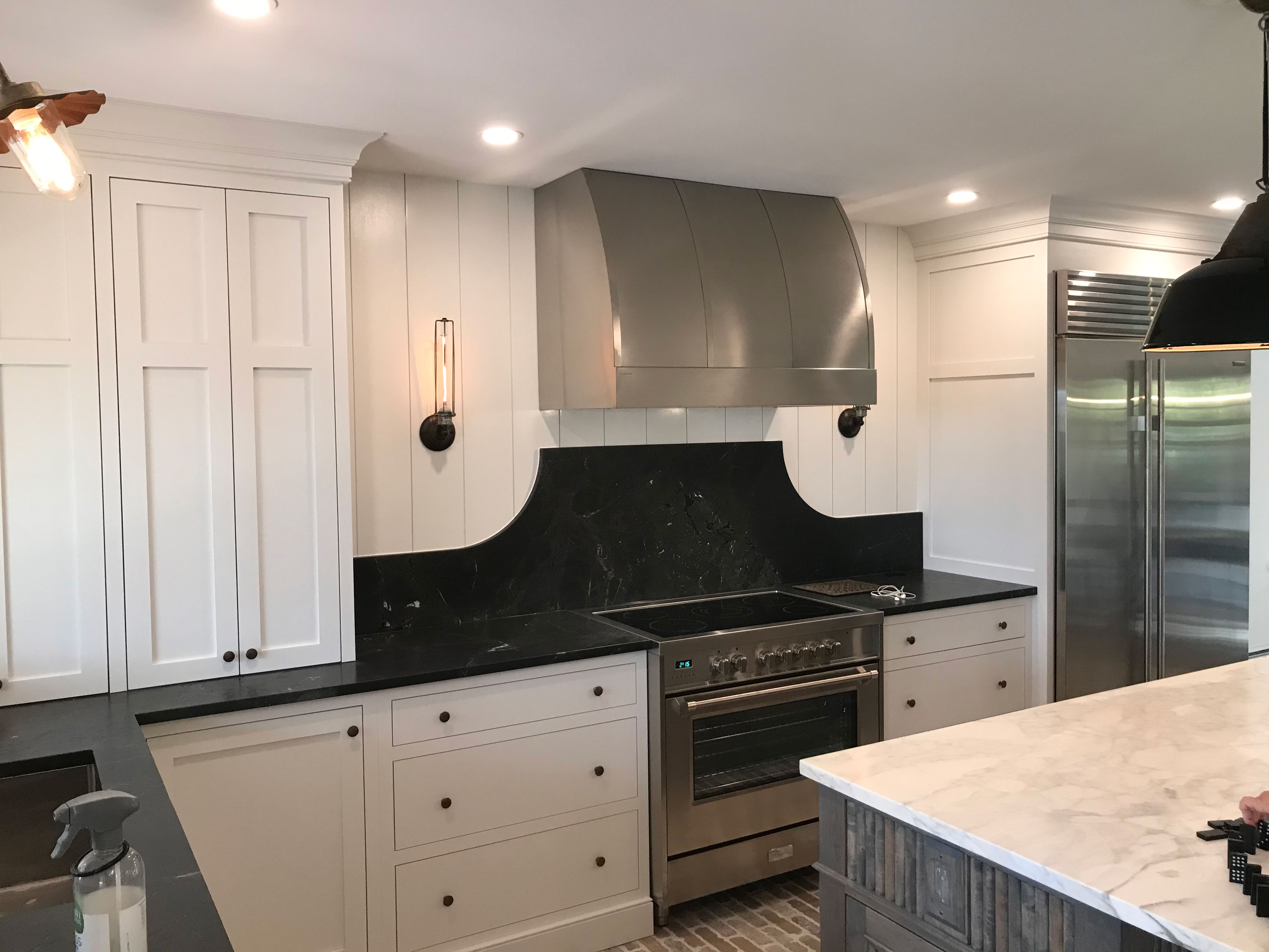 Silver stainless steel range hood in a kitchen with white cabinets and a tiled backsplash World CopperSmith