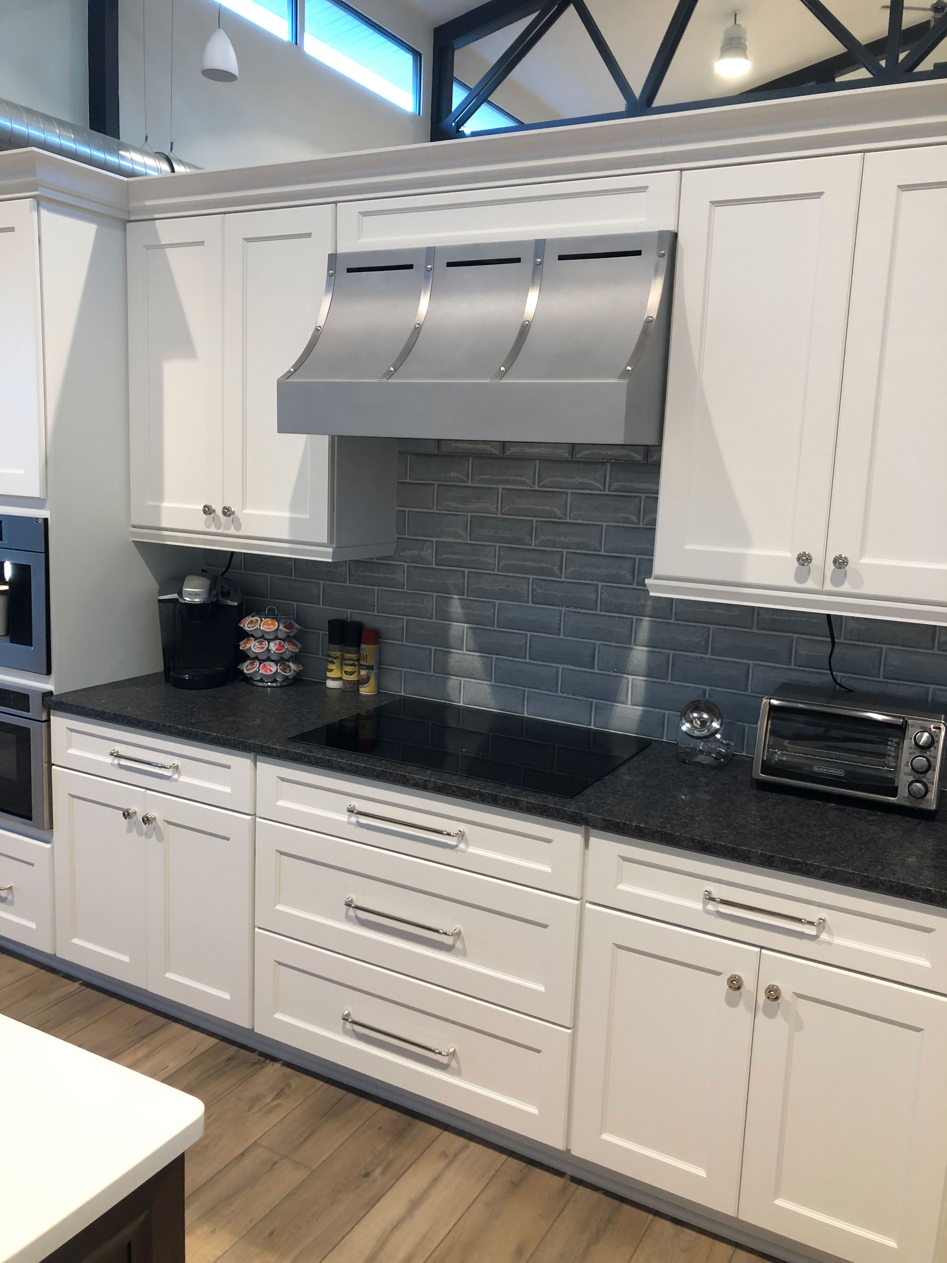 Classic kitchen design featuring with unique range hood, white kitchen cabinets, black kitchen countertops, brick backsplash