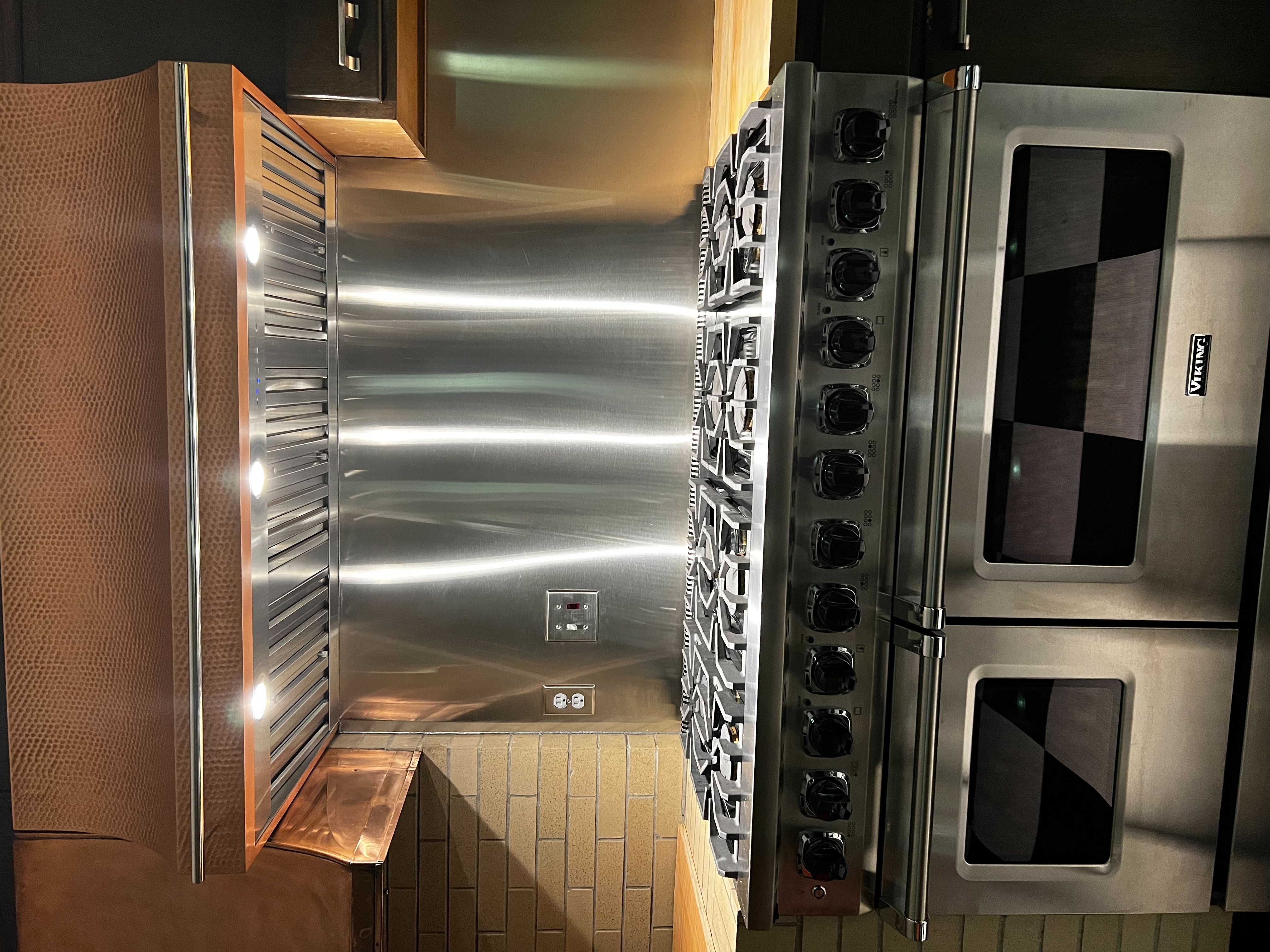 A coastal kitchen project with stylish range hood brown kitchen cabinets, stone kitchen countertops, metal backsplash