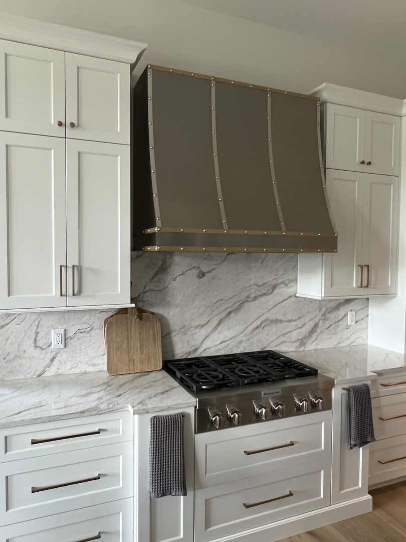 French kitchen design featuring range hood, white cabinets,sleek black countertops marble backsplash