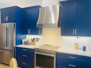 A coastal kitchen project with blue kitchen cabinets, white kitchen countertops, white tile backsplash complemented by a stylish range hood