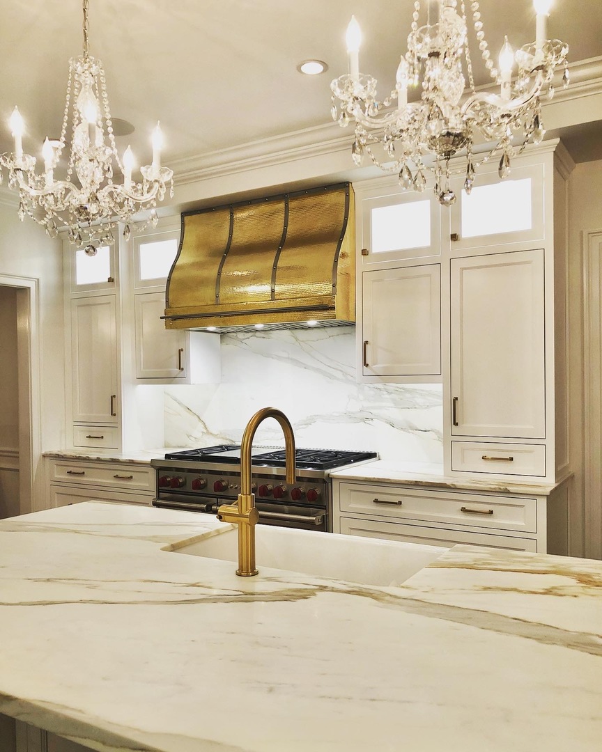 Brass range hood in white kitchen with wood floor and marble backsplash World CopperSmith
