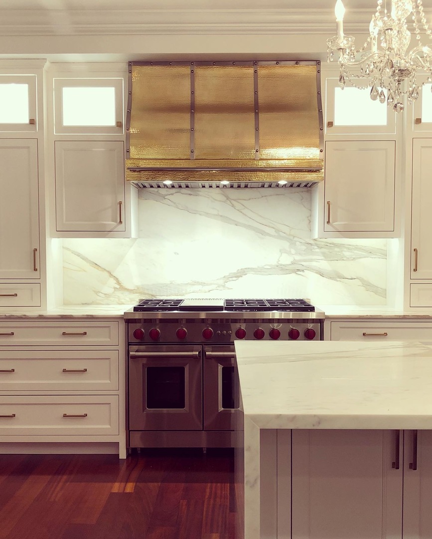Classic design idea featuring range hood, white cabinets,luxurious marble countertops with marble backsplash