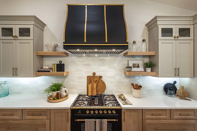 CopperSmith Premier PR8 Wall Mount Black Enamel Stainless Steel Range Hood with Matte Brass Straps and Rivets in a traditional style kitchen with wood cabinetry white countertops and white tile backsplash