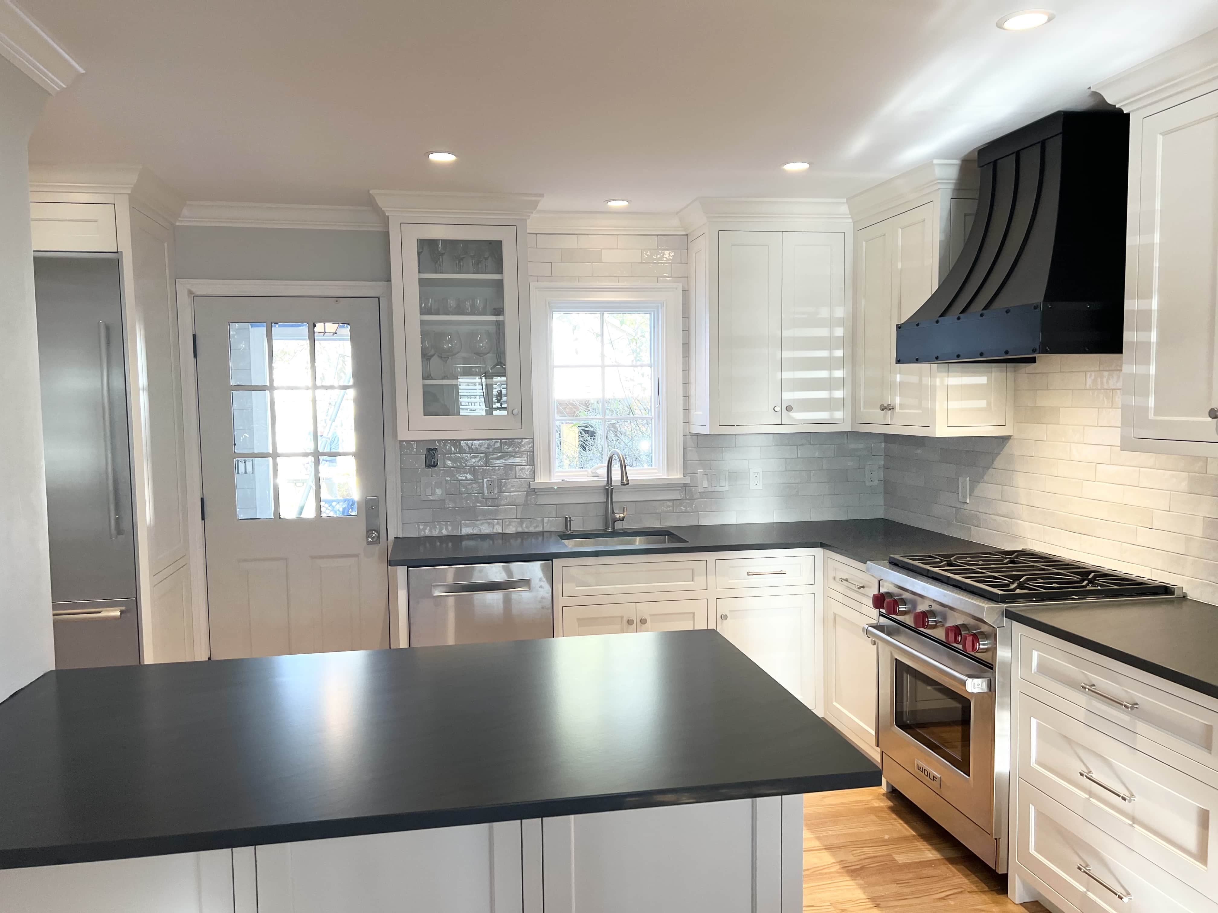 Chic french kitchen design ,sleek white cabinets, black countertops, captivating brick backsplash crowned by range hood