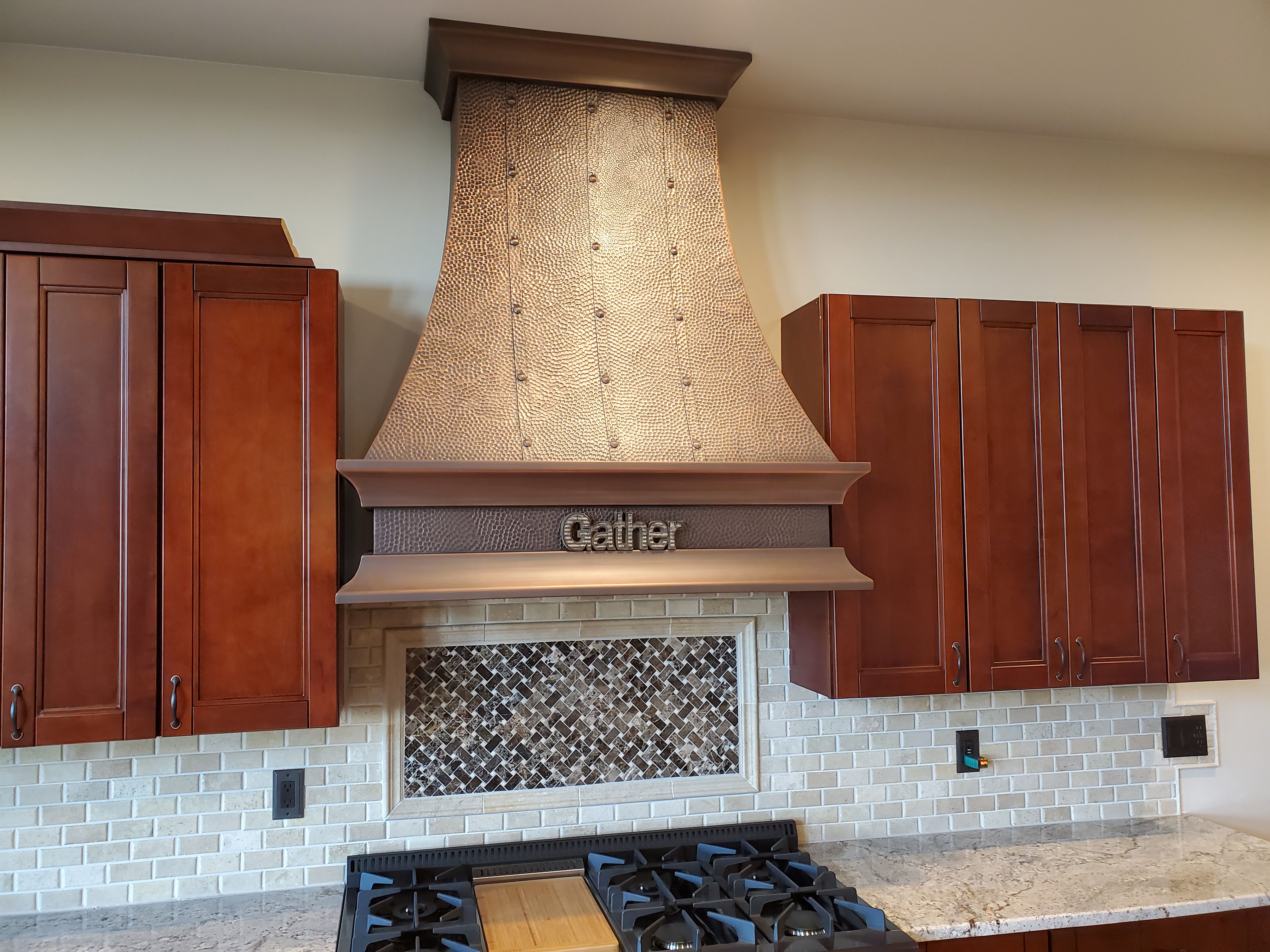Contemporary copper range hood with modern industrial kitchen renovation featuring brown kitchen cabinets, sleek marble countertops
