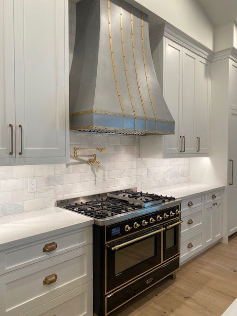 A classic kitchen design, consider pairing white kitchen cabinets and countertops with a sleek range hood, complemented by a charming brick backsplash