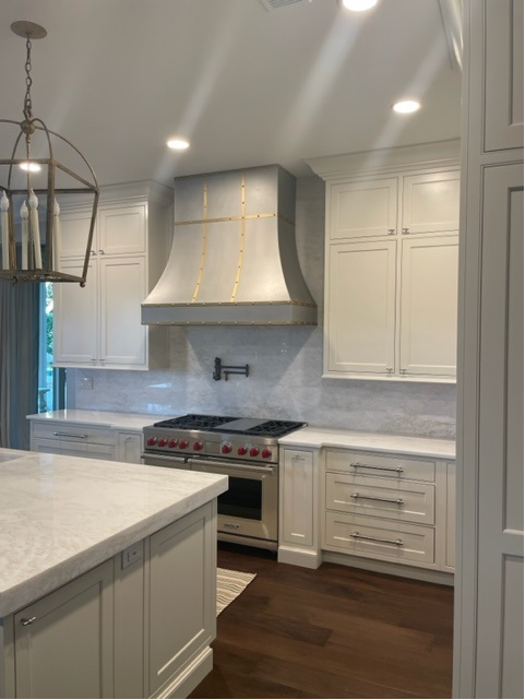A beautiful traditional kitchen with white cabinets, white countertops, stunning marble backsplash, complete with a stylish range hood