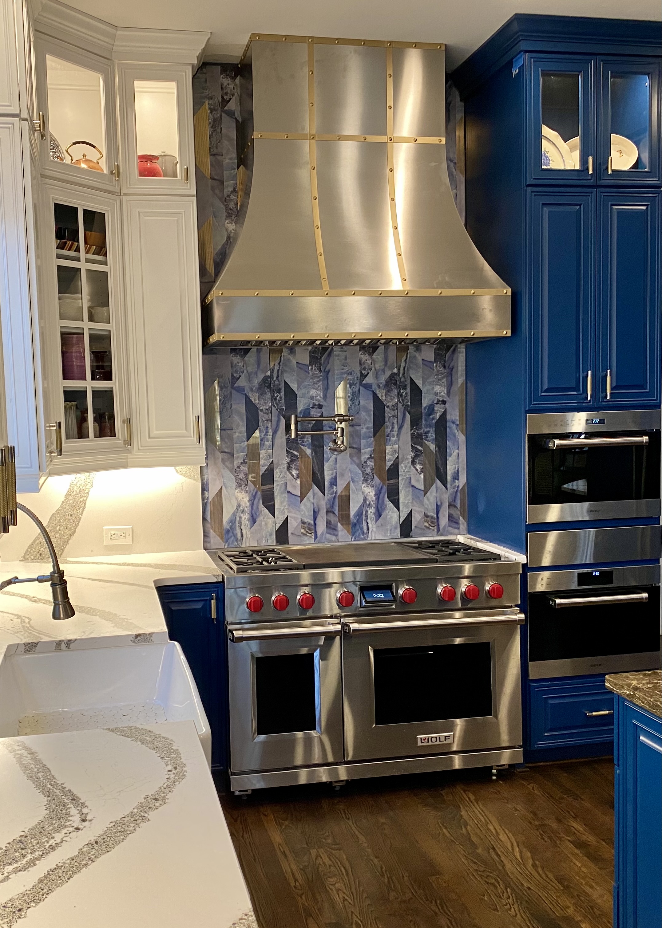 A sleek industrial kitchen renovation featuring blue kitchen cabinets, marble kitchen countertops, a stunning marble backsplash, stylish range hood