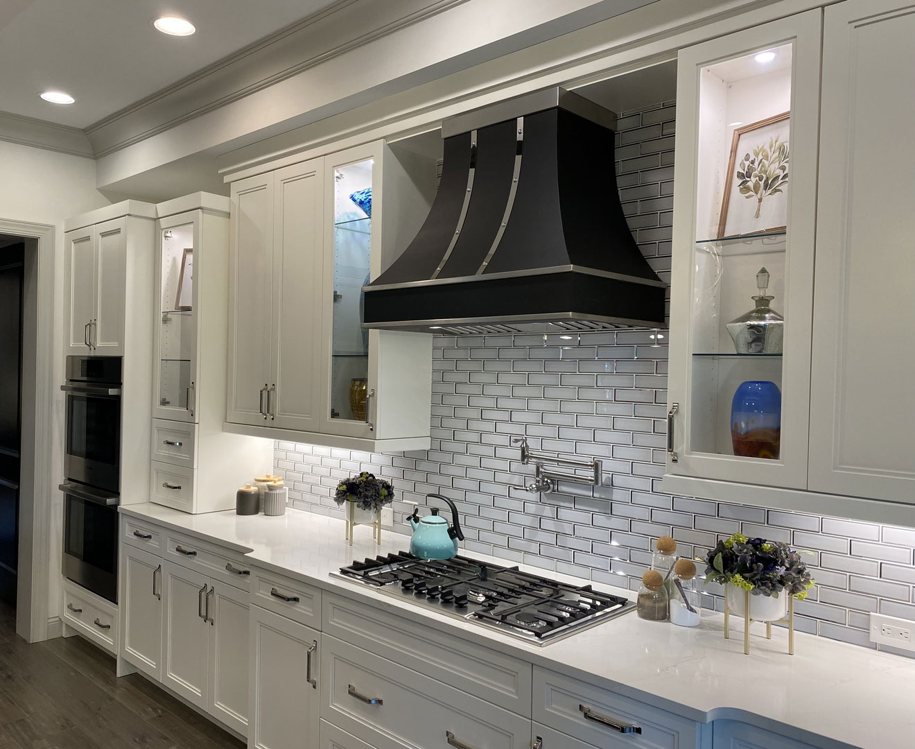 Classic kitchen with white cabinets and countertops, complemented by a brick backsplash sleek range hood, creates a timeless and stylish design