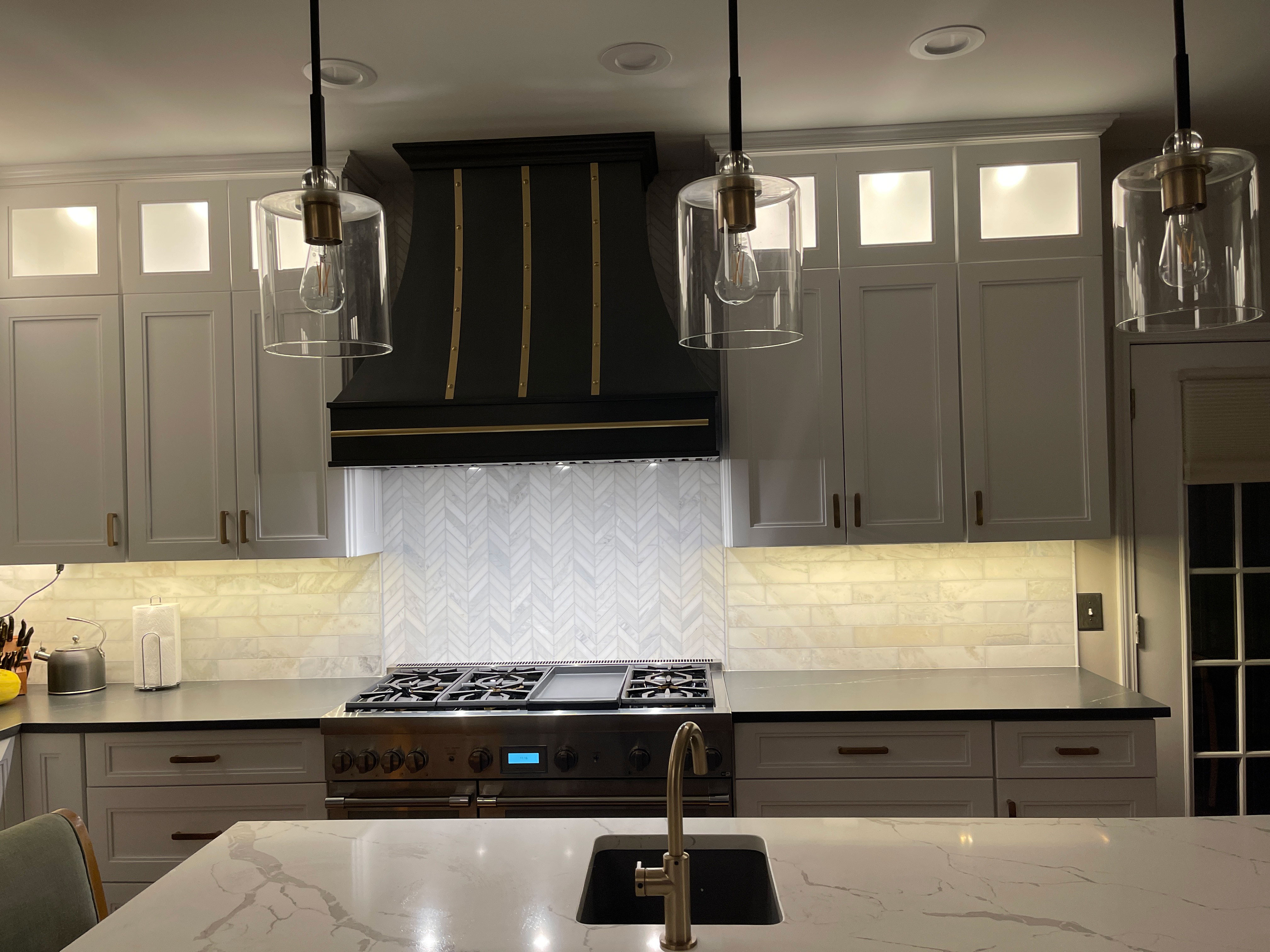 Modern kitchen with white cabinets, grey countertops, stylish brick backsplash, complemented by a chic range hood