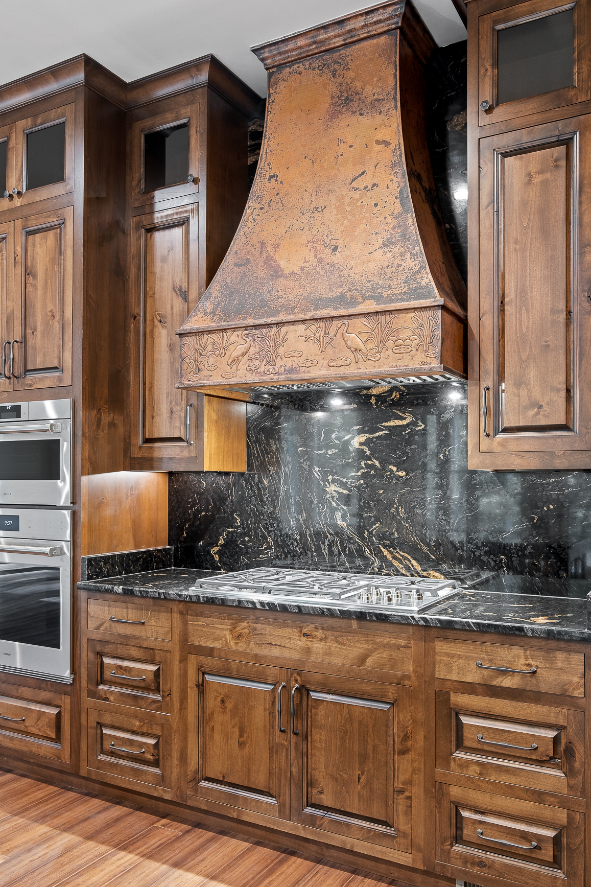 A stunning french kitchen featuring stylish range hood, wood kitchen cabinets, black kitchen countertops, marble backsplash