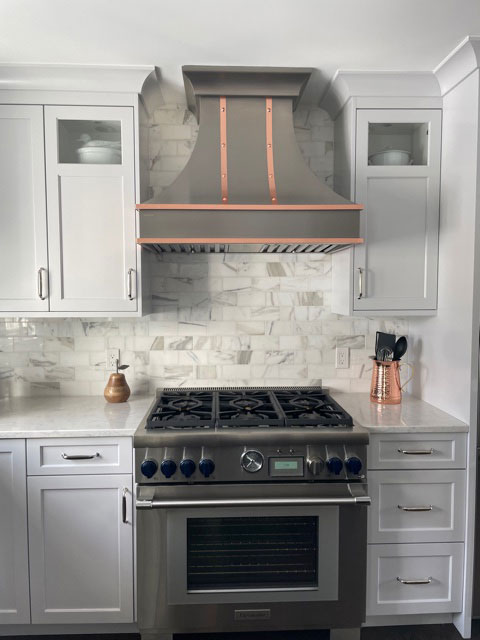 Timeless kitchen design with white cabinets, elegant marble countertops, stunning brick backsplash, complemented by a stylish range hood