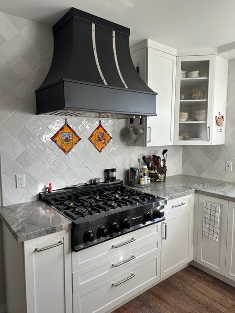 Beautiful cottage kitchen with white kitchen cabinets, marble countertops, white tile backsplash, complemented by a stylish range hood