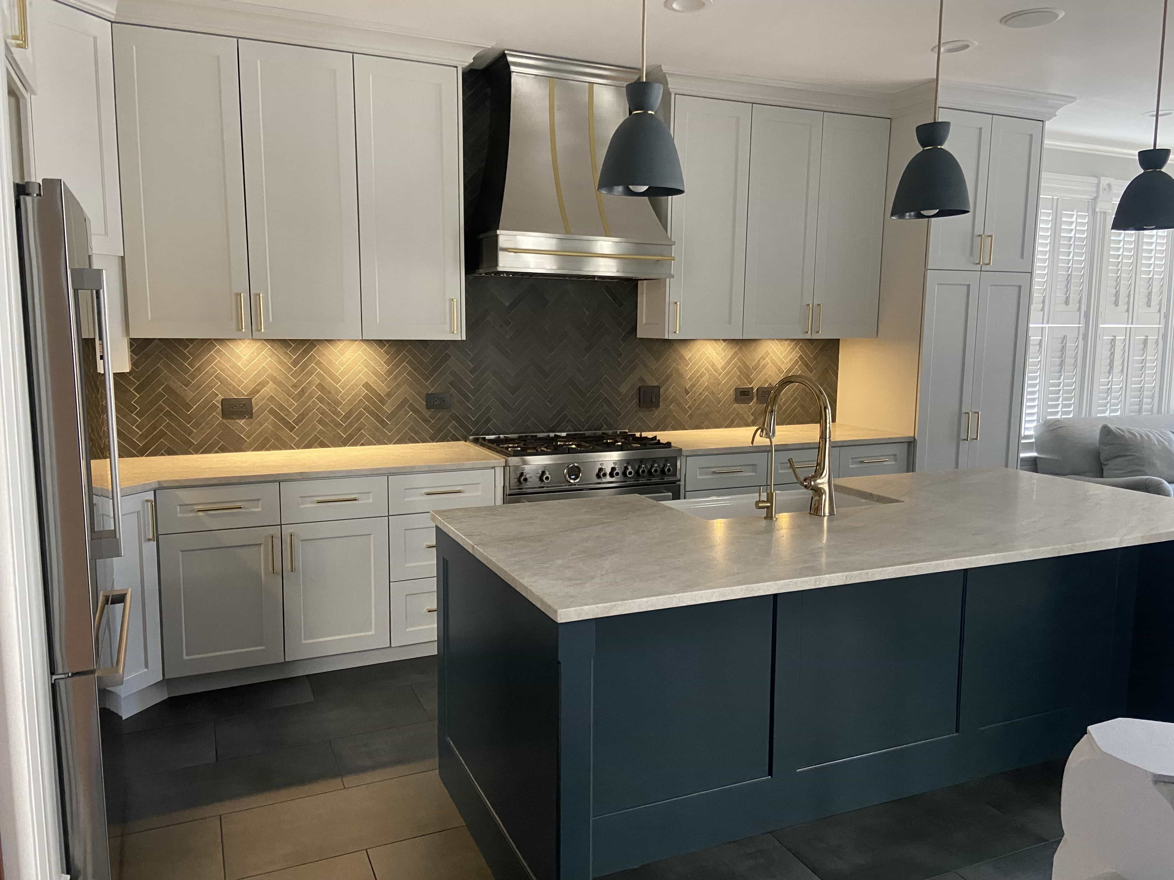 CopperSmith Signature SX4 Brushed Stainless Steel Range Hood in a contemporary kitchen featuring blue and white cabinets white countertops and back tile backsplash