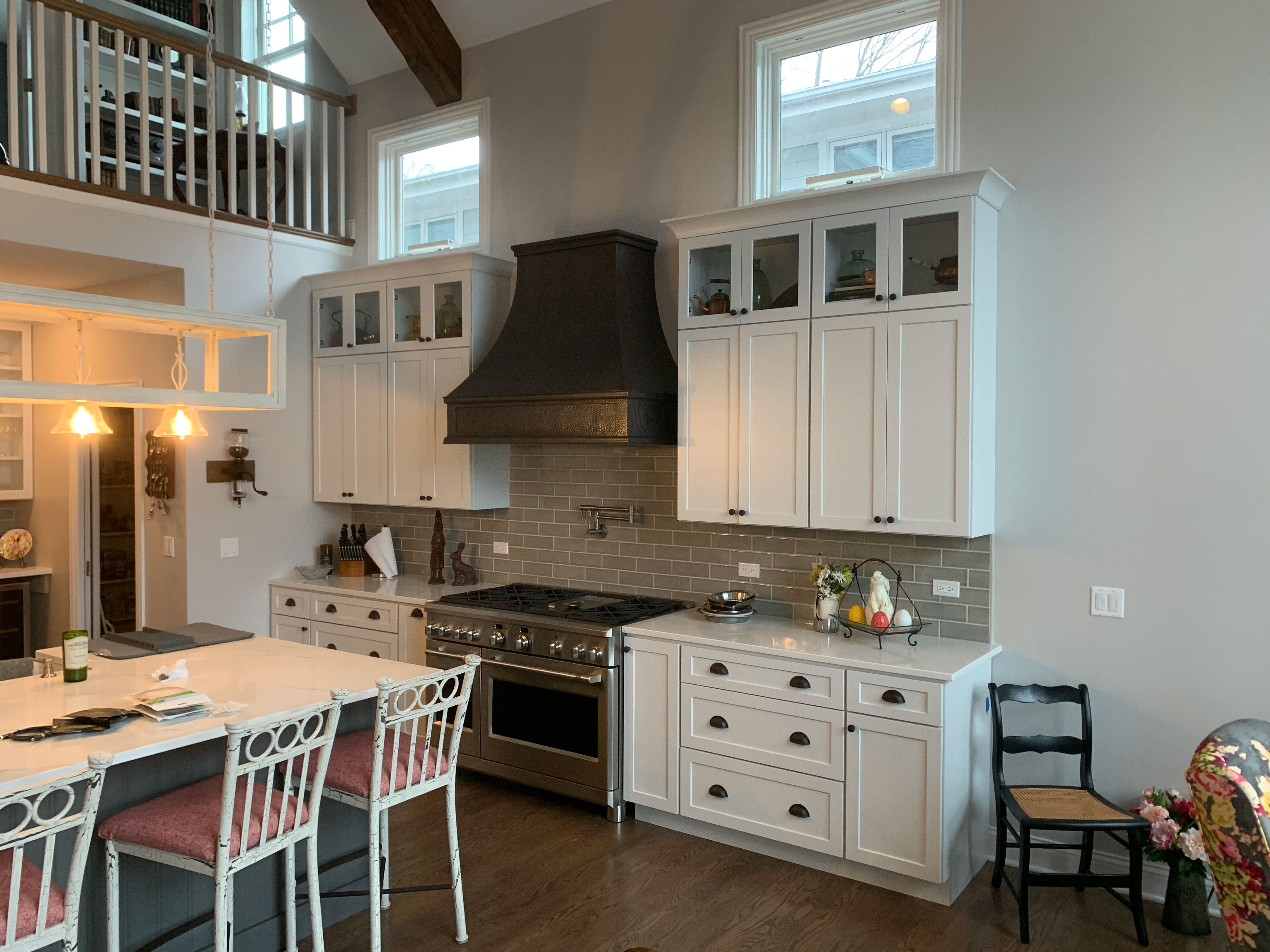 A coastal-inspired kitchen with sleek range hood, white cabinets, white countertops, charming brick backsplash