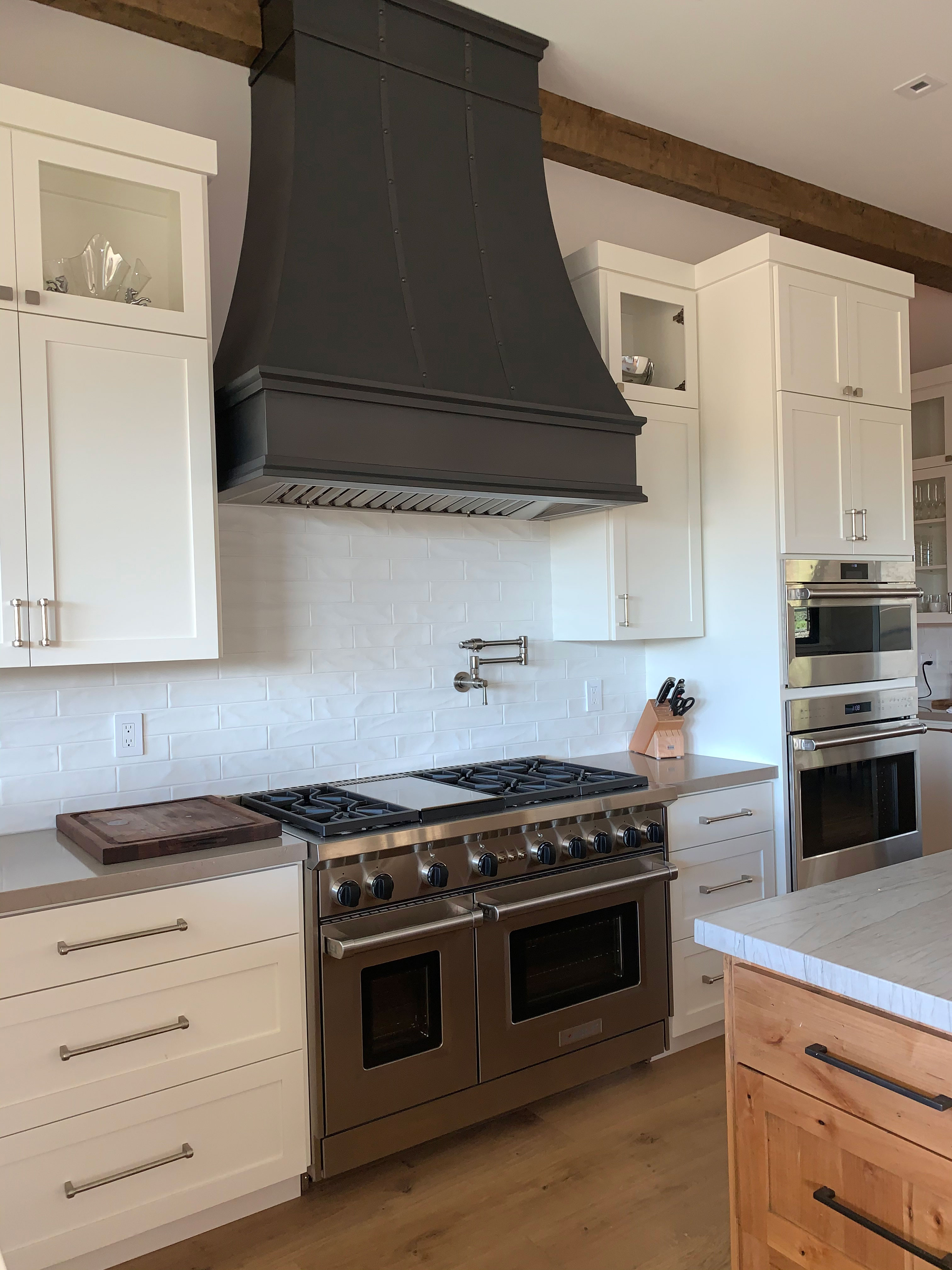 A harmonious and stylish kitchen design with stylish range hood, coastal kitchen project with white kitchen cabinets, marble kitchen countertops, stunning brick backsplash