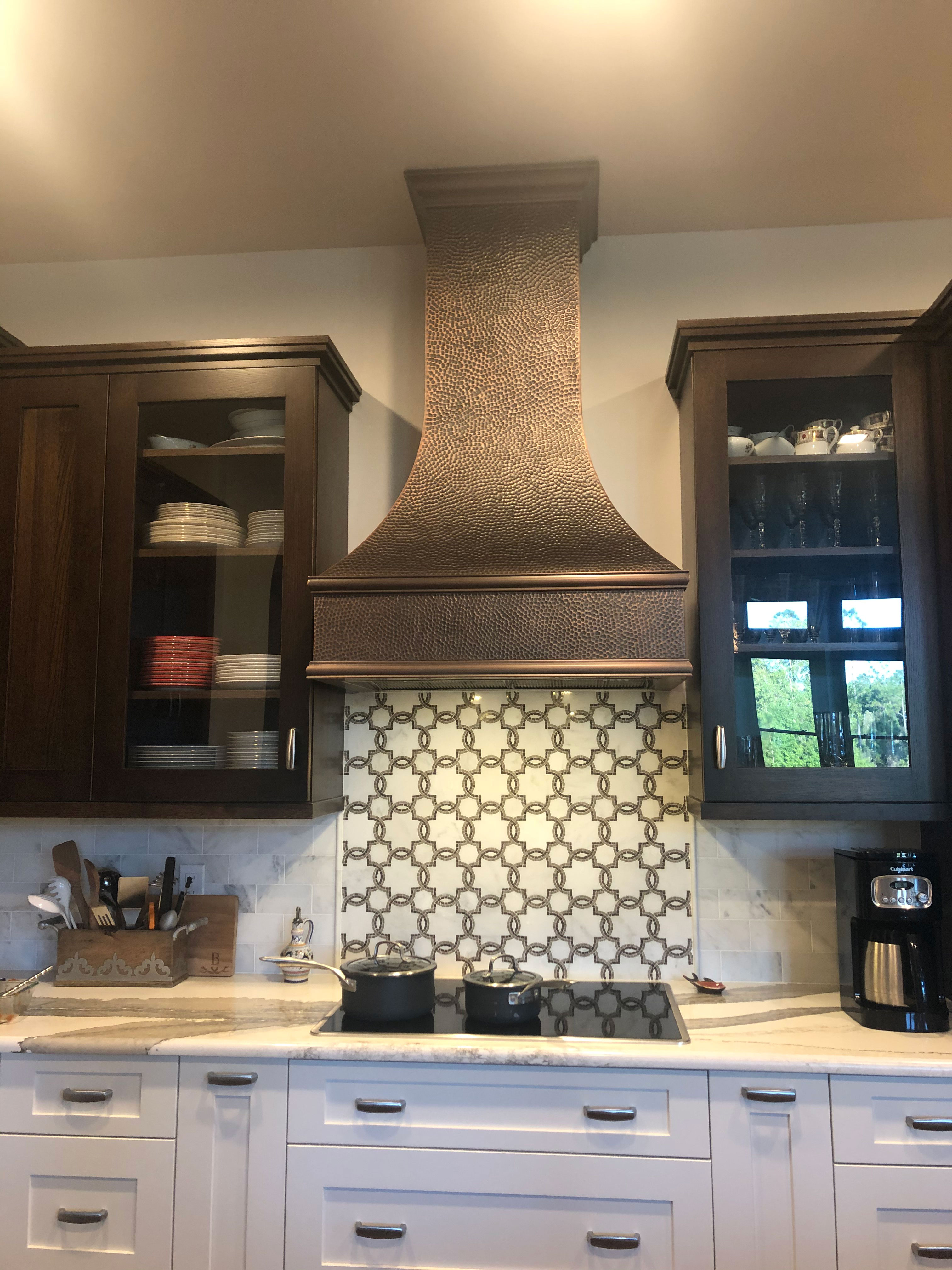 Kitchen with a copper sleek range hood, elegant french design, pristine white cabinets, luxurious marble countertops, charming brick backsplash