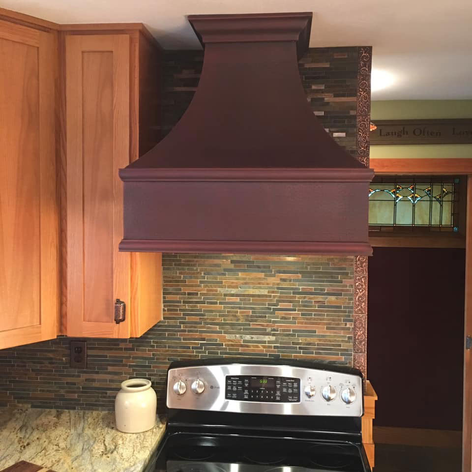Red copper range hood in kitchen with wood cabinets and tile backsplash