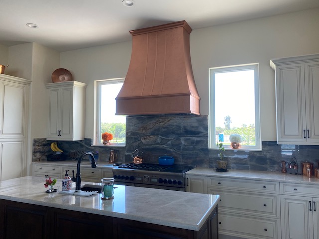 CopperSmith Signature SX5 Wall Mount Range Hood Old Coin Copper Finish with straps in a contemporary kitchen with white countertops white cabinets and tile backsplash