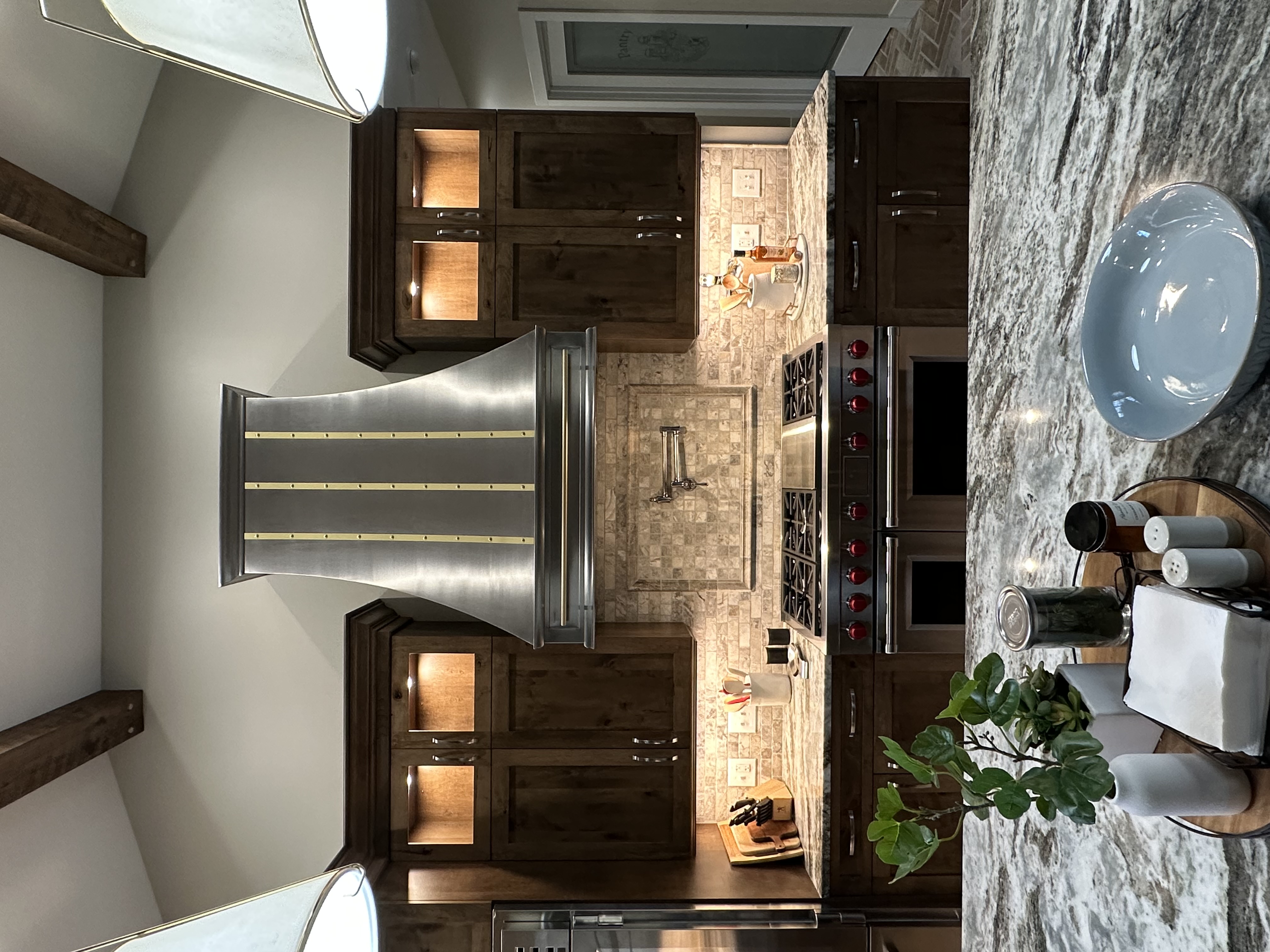 Beautiful range hood french kitchen design, accentuated by rich brown kitchen cabinets, marble kitchen countertops, and marble backsplash