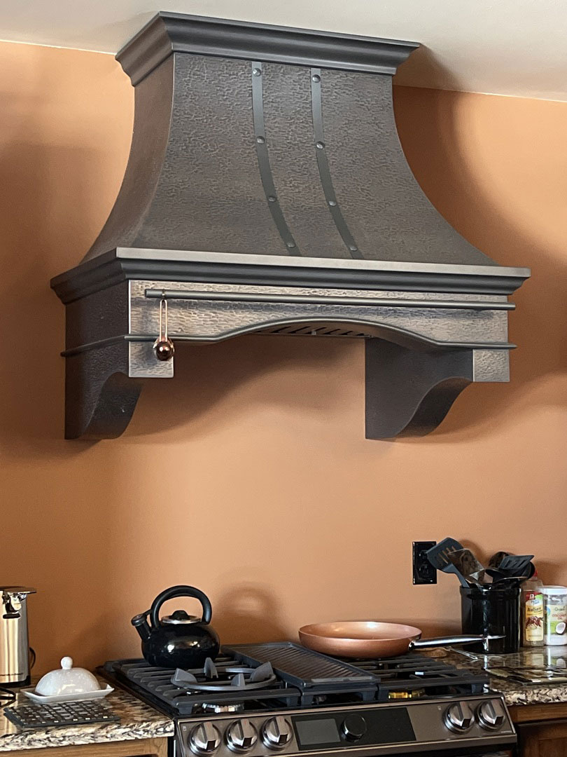 Gray copper hood with belts and bolts in kitchen with copper wall