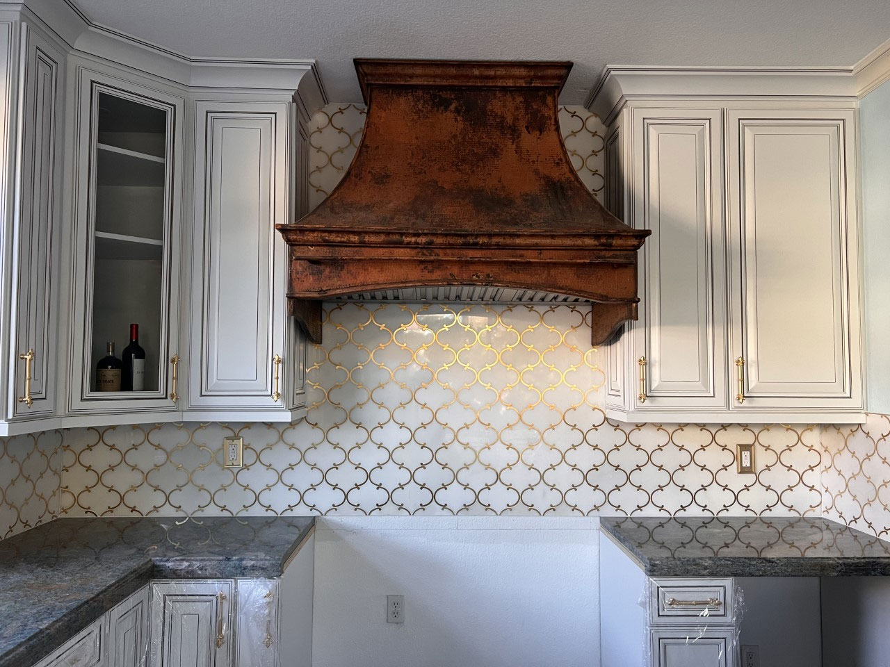 Stylish range hood complemented with a classic kitchen design with white cabinets, marble countertops, stunning marble backsplash